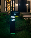 Caixa de correio Itu preta com iluminação LED azul acesa à noite em fachada residencial
