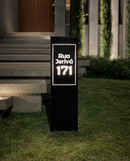 Totem de endereço Malta preto com iluminação LED acesa à noite em jardim de fachada residencial
