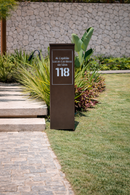 Totem personalizado Malta marrom em ACM instalado em jardim com pedras durante o dia
