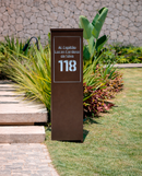 Totem residencial Malta marrom corten em ACM personalizado em jardim tropical durante o dia
